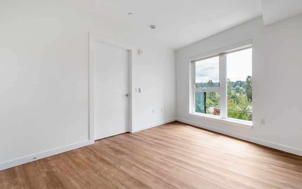 a bedroom with a window, wood floors and white walls